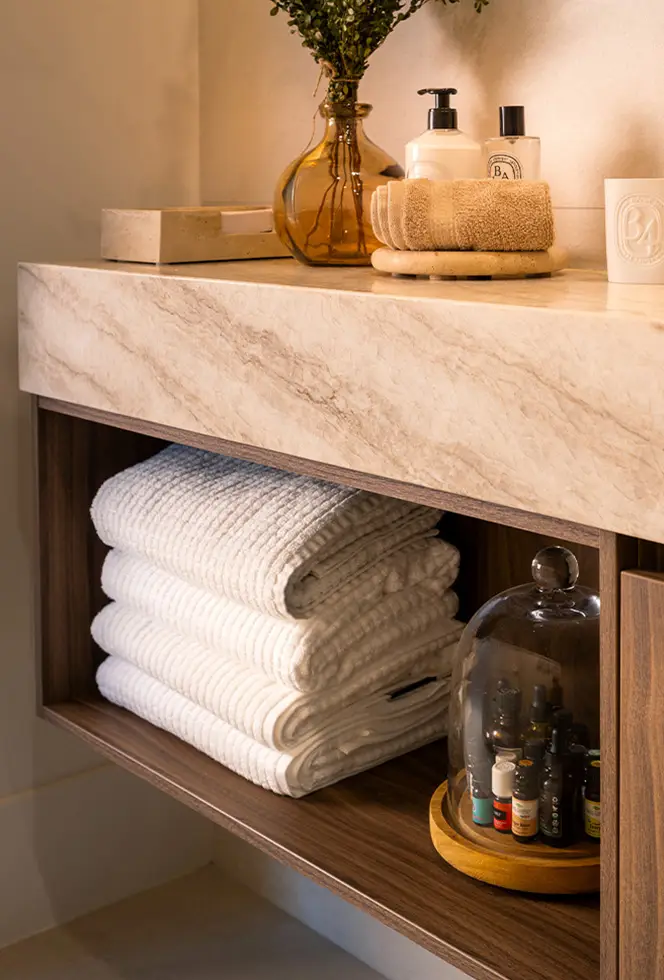 Stone bathroom vanity with open shelving beneath, holding folded towels