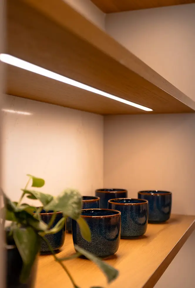 Under-cabinet lighting across an oak shelf with ceramics and a plant