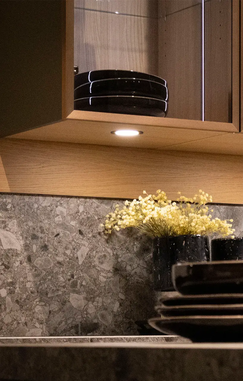 Under-cabinet lighting washing a stone worktop beside a wood-fronted wall unit